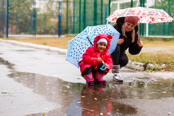 傘の下で公園で赤いコートで幼い娘を持つ若い女性 — ストック写真