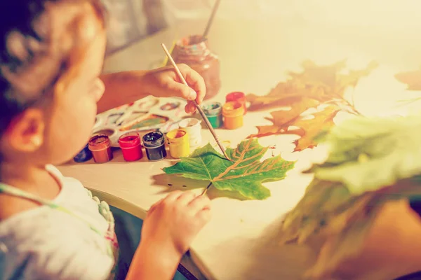 little girl drawing with paint autumn leaves at home