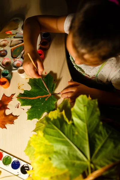 little girl drawing with paint autumn leaves at home