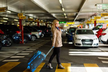 Bagajlı genç bayan turist havaalanındaki otoparktan geçiyor.