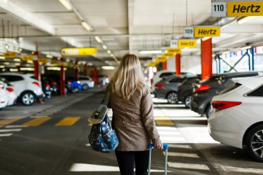 Bagajlı genç bayan turist havaalanındaki otoparktan geçiyor.