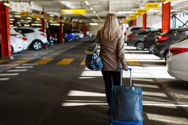 Bagajlı genç bayan turist havaalanındaki otoparktan geçiyor.