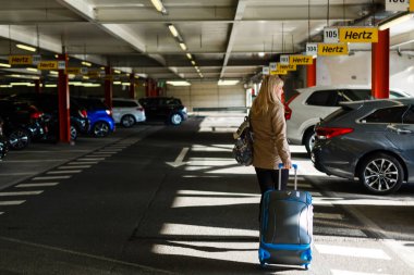 Bagajlı genç bayan turist havaalanındaki otoparktan geçiyor.