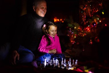 Dede torunu yazlık dekore edilmiş şömine ve Noel ağacı yakınındaki satranç oynamak için öğretim