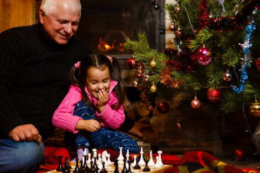 Dede torunu yazlık dekore edilmiş şömine ve Noel ağacı yakınındaki satranç oynamak için öğretim