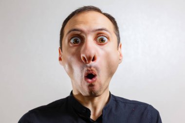 Gri arka planda poz veren yüzünde grimace olan genç beyaz adamın portresi 