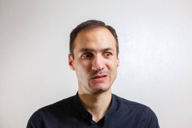 Gri arka planda poz veren yüzünde grimace olan genç beyaz adamın portresi 