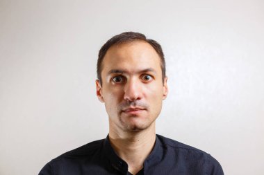 Gri arka planda poz veren yüzünde grimace olan genç beyaz adamın portresi 