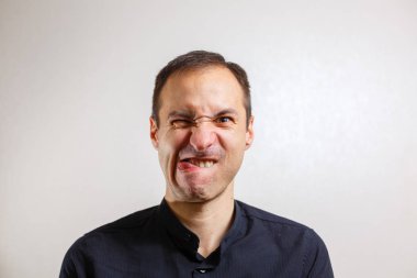Gri arka planda poz veren yüzünde grimace olan genç beyaz adamın portresi 