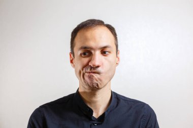 Gri arka planda poz veren yüzünde grimace olan genç beyaz adamın portresi 