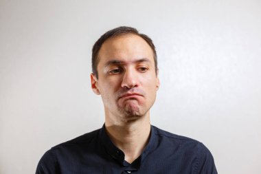 Gri arka planda poz veren yüzünde grimace olan genç beyaz adamın portresi 