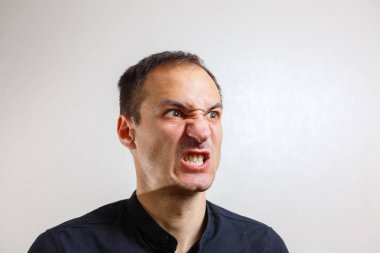 Gri arka planda poz veren yüzünde grimace olan genç beyaz adamın portresi 