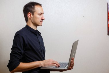 Gri arka planda dizüstü bilgisayar tutan genç adam 