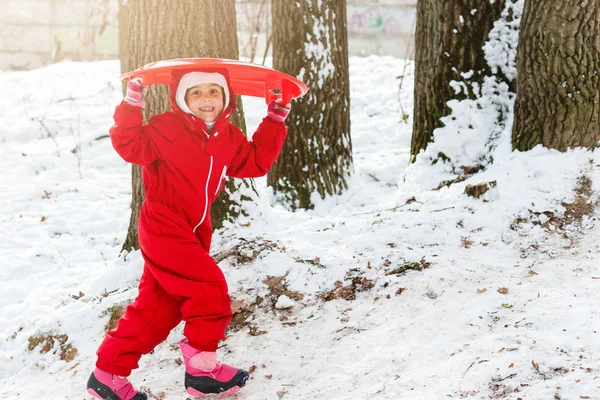 微笑的女孩在红色滑雪服滑下雪覆盖的山与雪橇 — 图库照片