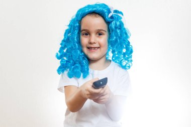 Beyaz arka planda tv-remote tutan mavi dolly peruk küçük kız 