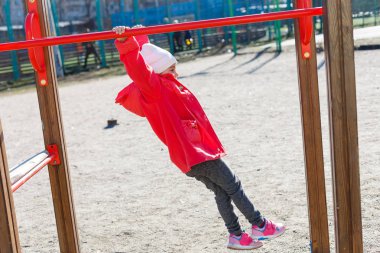Kırmızı ceketli aktif küçük kız oyun alanında eğleniyor
