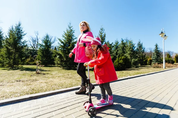 スクーターに乗っている小さな女の子と公園の横を歩く母親 — ストック写真