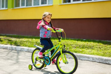 Binanın etrafında bisiklete binen gülümseyen küçük kız 