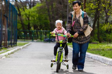 Mutlu genç anne bisiklete binmek için küçük kızı öğretim