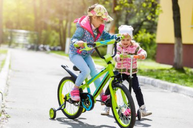 Yeşil bahar parkında scooter ve bisiklete binen mutlu kızlar