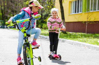 Yeşil bahar parkında scooter ve bisiklete binen mutlu kızlar
