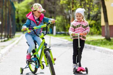 Yeşil bahar parkında scooter ve bisiklete binen mutlu kızlar