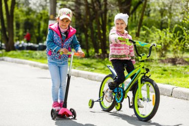 Yeşil bahar parkında scooter ve bisiklete binen mutlu kızlar