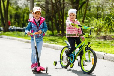Yeşil bahar parkında scooter ve bisiklete binen mutlu kızlar