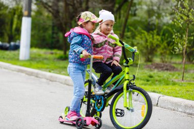 Yeşil bahar parkında scooter ve bisiklete binen mutlu kızlar