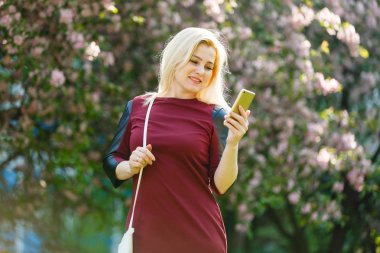 bahar çiçek açan parkta smartphone kullanarak sarışın genç kadın portresi