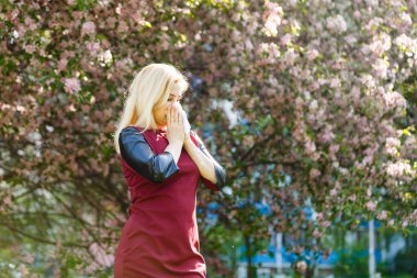 Genç kadın çiçek açan ağaç önünde burun üfleme