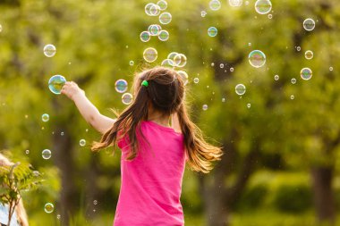 Yeşil bahçede sabun kabarcıkları ile oynayan neşeli kız