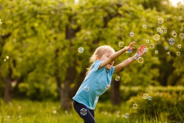 Yeşil bahçede sabun kabarcıkları ile oynayan neşeli kız