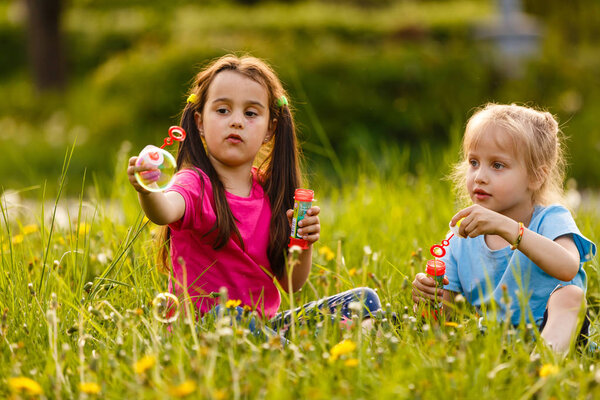 Little girls blowing soap bubbles in green park at sunset