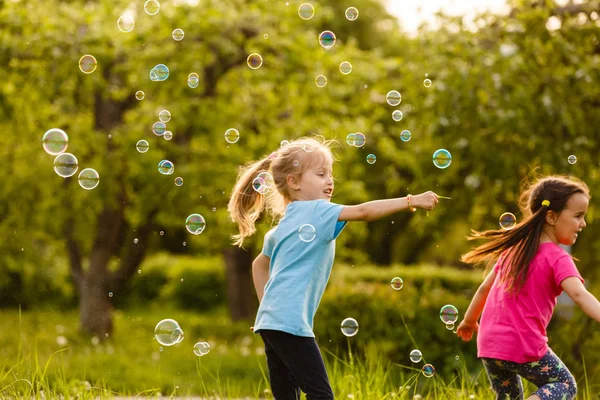 两个女孩很高兴在日落时在绿色公园漂浮肥皂泡 — 图库照片