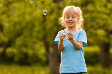 Yeşil bahçede sabun kabarcıkları ile oynayan neşeli kız