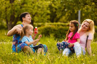 Kızları yeşil parkta sabun kabarcıkları üfleme anneler
