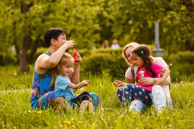 Kızları yeşil parkta sabun kabarcıkları üfleme anneler