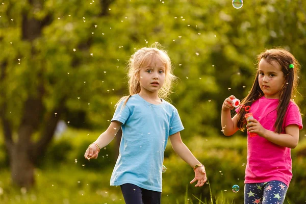两个女孩在绿色公园玩耍 吹漂浮的肥皂泡 — 图库照片