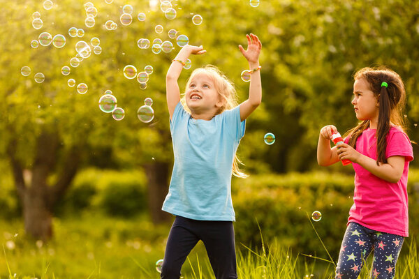 Two girls playing in green park and blowing floating soap bubbles
