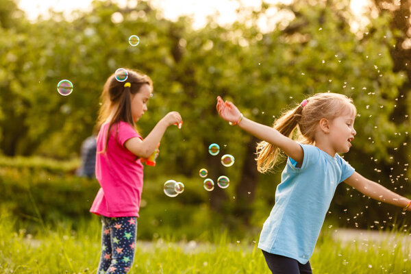 Two girls playing in green park and blowing floating soap bubbles