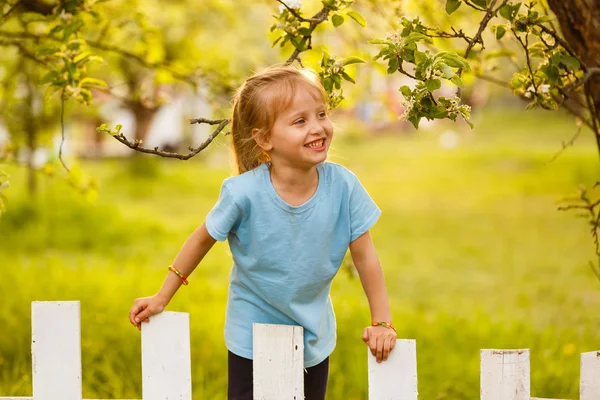 Kleines Mädchen Steht Bei Sonnenuntergang Hinter Weißem Holzzaun Garten — Stockfoto