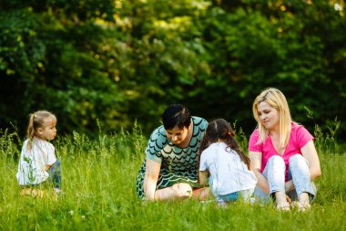 Yeşil parkta dinlenmiş okul öncesi kızları olan iki anne