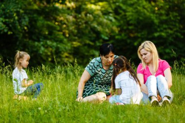 Yeşil parkta dinlenmiş okul öncesi kızları olan iki anne