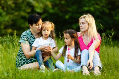 Yeşil parkta dinlenmiş okul öncesi kızları olan iki anne