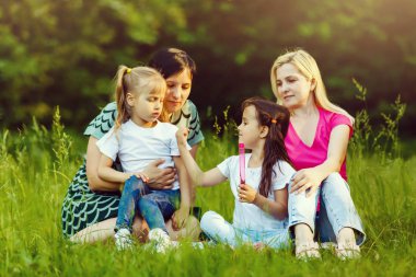 Yeşil parkta dinlenmiş okul öncesi kızları olan iki anne
