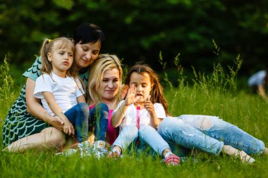 Yeşil parkta dinlenmiş okul öncesi kızları olan iki anne