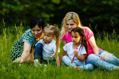 Yeşil parkta dinlenmiş okul öncesi kızları olan iki anne