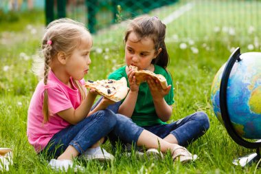 Çimenlerin üzerinde oturan ve taze pizza yemek iki kız