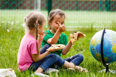 Çimenlerin üzerinde oturan ve taze pizza yemek iki kız